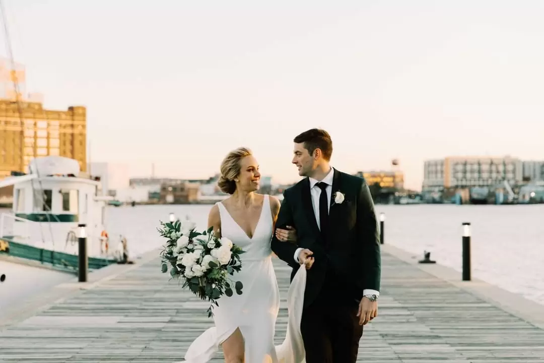Фото жених и невеста довольные идут по пирсу на фоне моря и кораблей