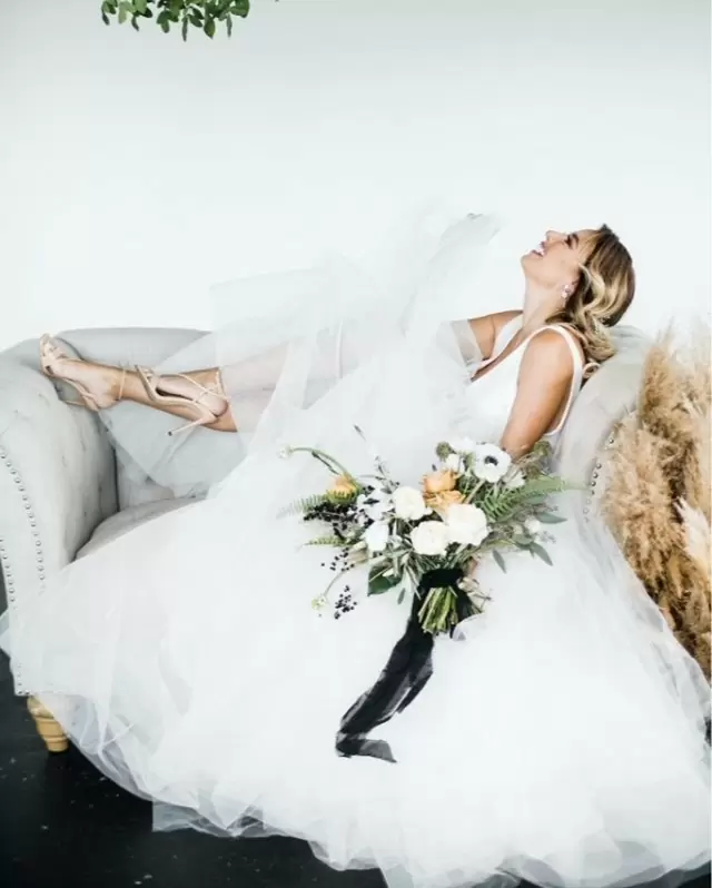 Невеста в свадебном платье чистейшего белого цвета Белоснежка (Snow white) с букетом розовых цветов лежит на диване.