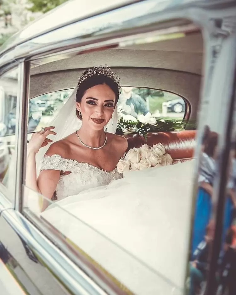 Фото невесты в машине с букетом цветов и красивым макияжем.
