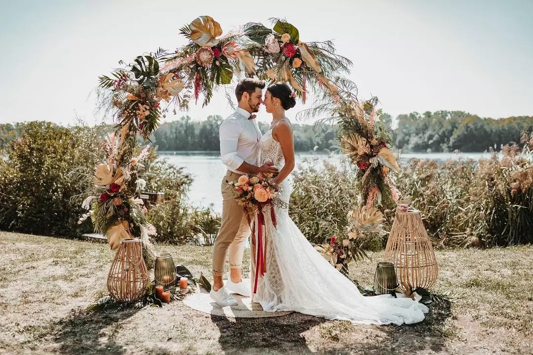 Фото. Жених и невеста около водоема на природе стоят на фоне свадебной арки в стиле рустик
