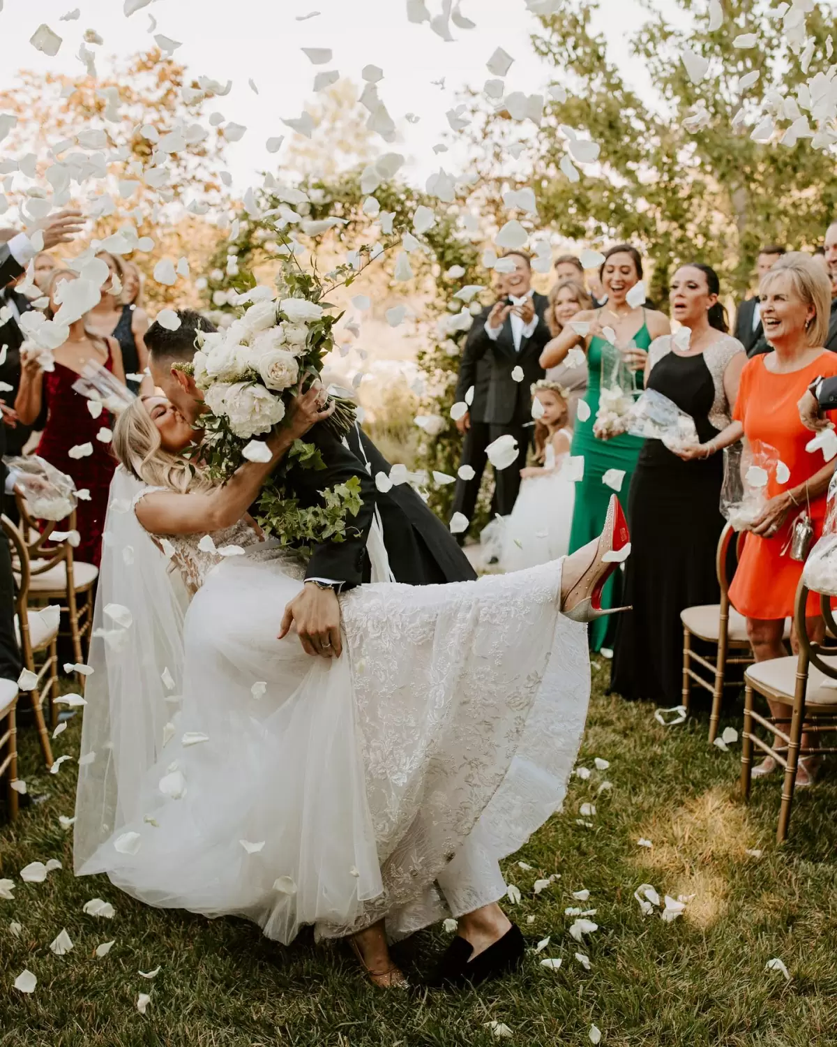 Фото. Жених и невеста целуются, а гости кидают в них лепестки цветов.