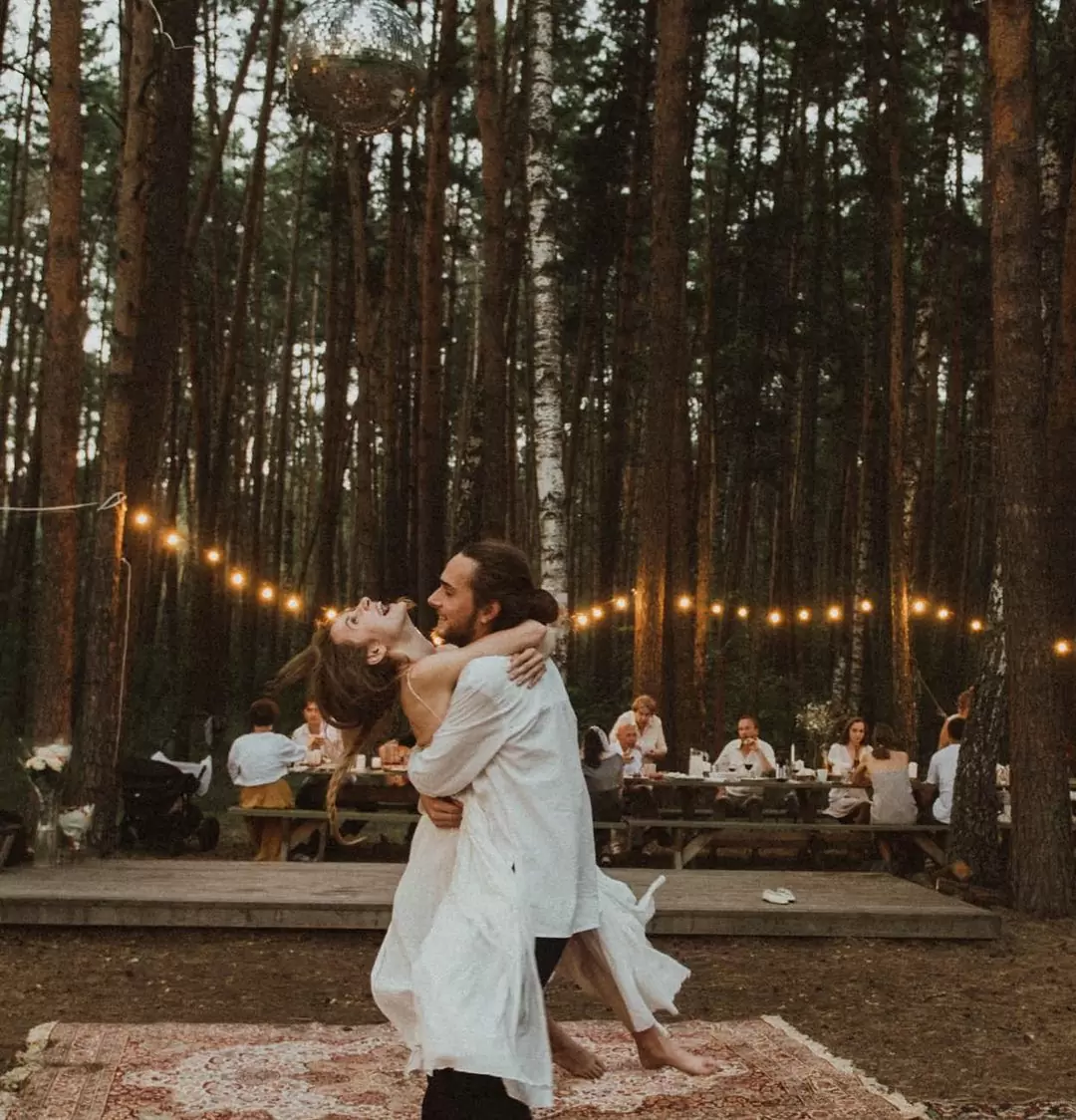 Жених и Невеста довольные, свободные и счастливые в лесу глэмпинга на фоне ковров и гирлянд