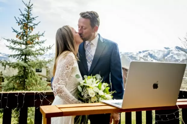 Фото. Мужчина и женщина проводят свадебную церемонию около монитора apple.