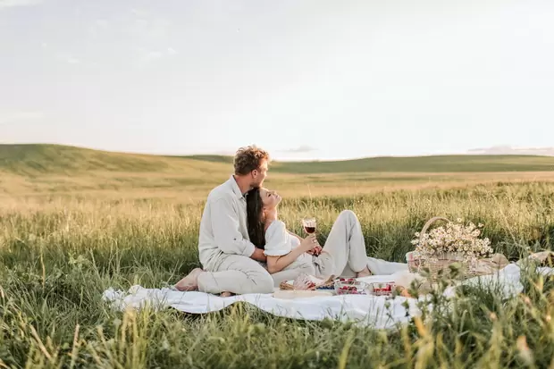 Девушка и мужчина на природе в белых одеждах пьют вино во время пикника.