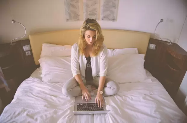 Девушка на кровати работает за ноутбуком