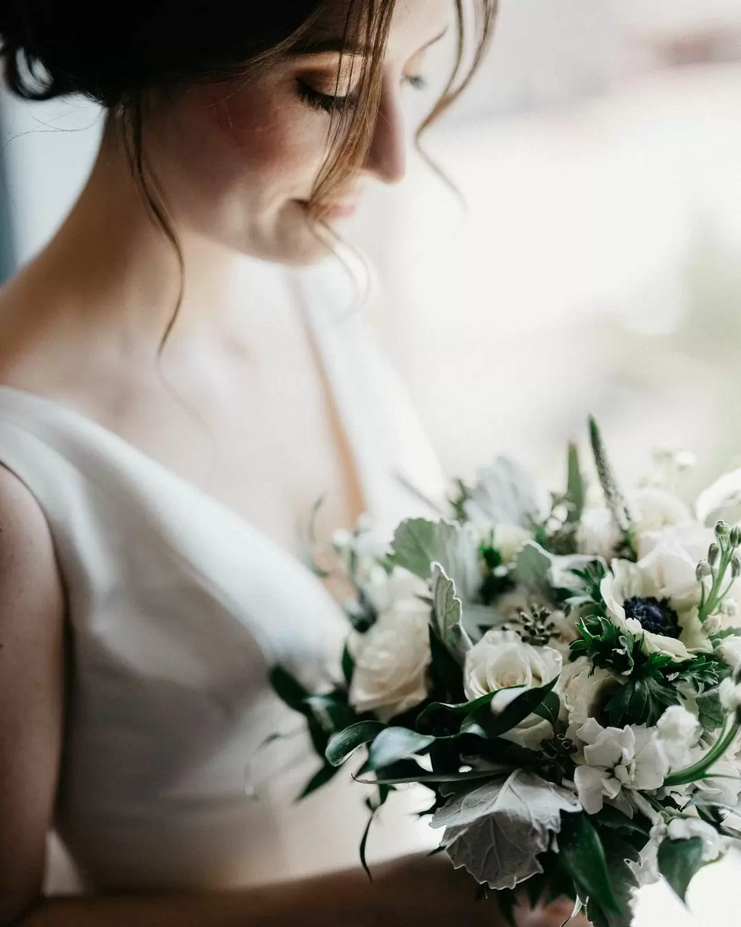 Невеста смотрит на букет из белых роз. 